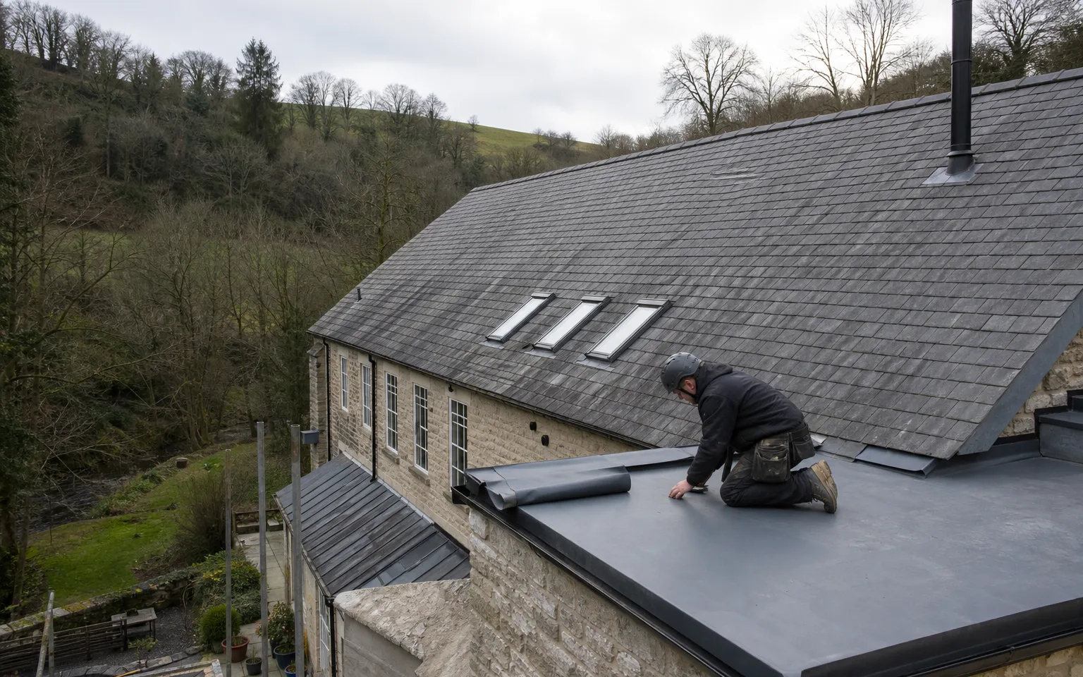Roofer fitting a grey single-ply membrane on a flat section of a stone mill roof