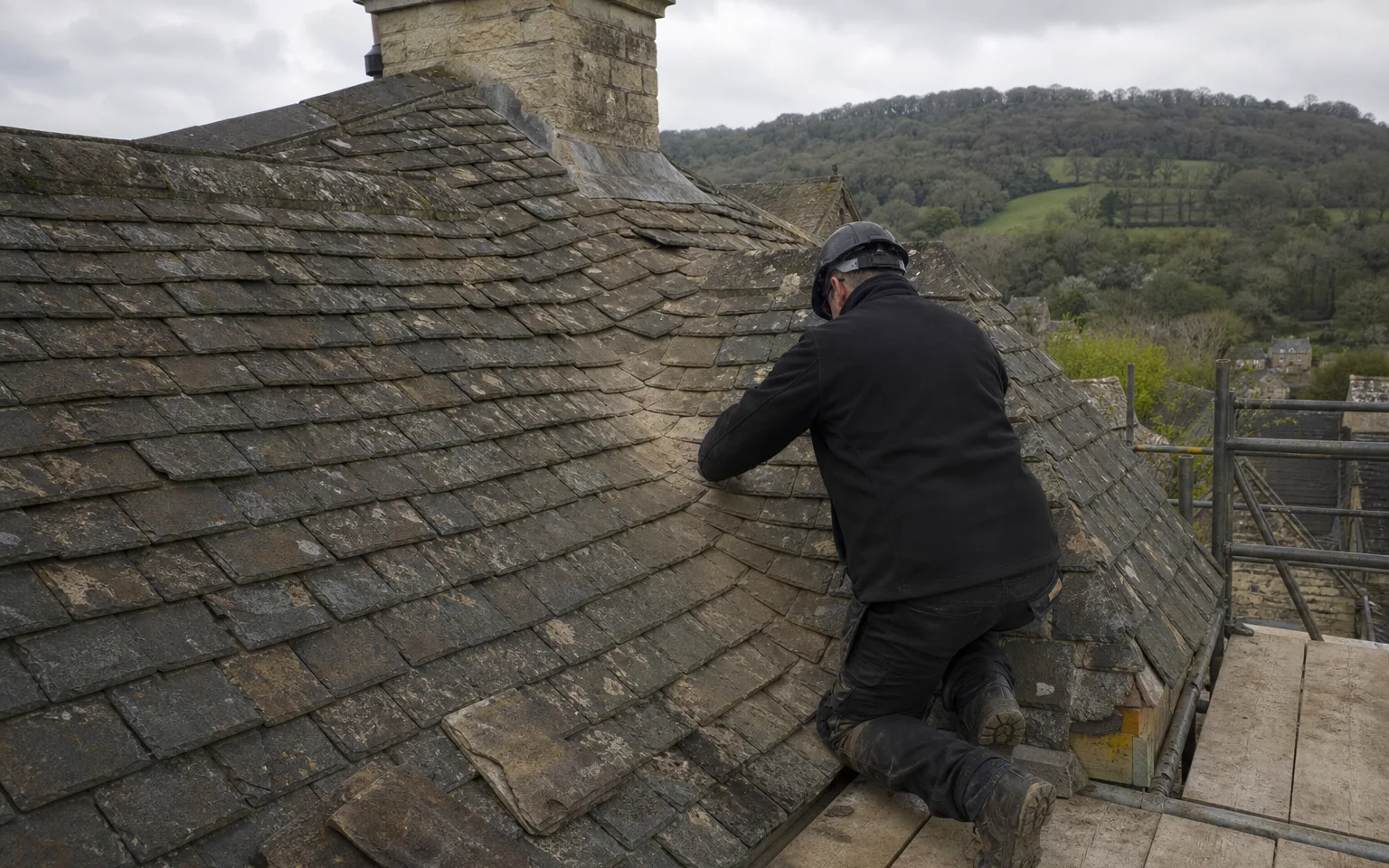 Roofer kneeling beside a swept valley of cut stone slates on a Cotswold roof