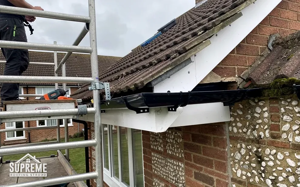 New white fascia, soffit and black gutter fitted under scaffolding on a flint house