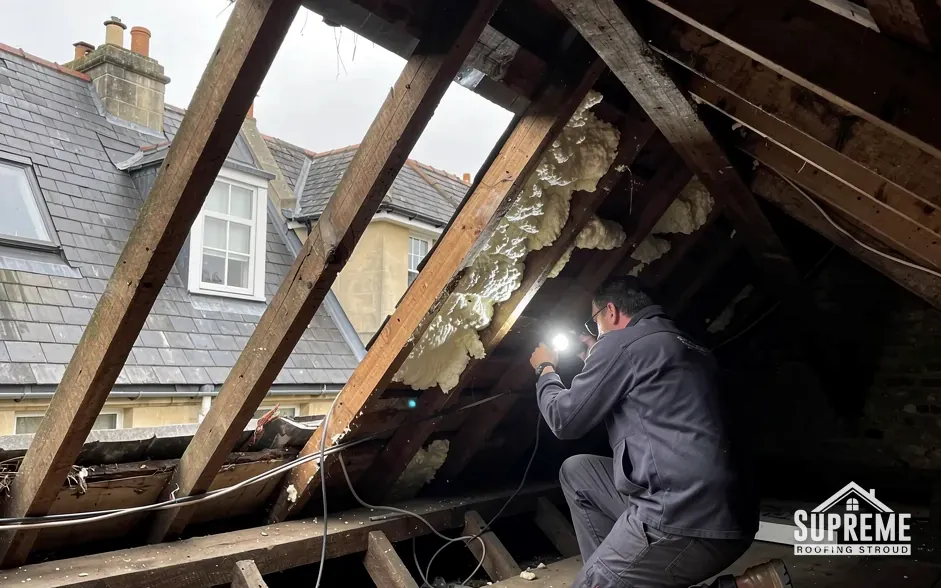 Surveyor with a torch inspecting rafters and insulation inside a loft