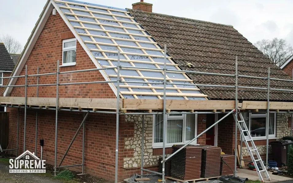 Roofers stripping an old tiled roof from scaffold on a terraced hillside street in Stroud