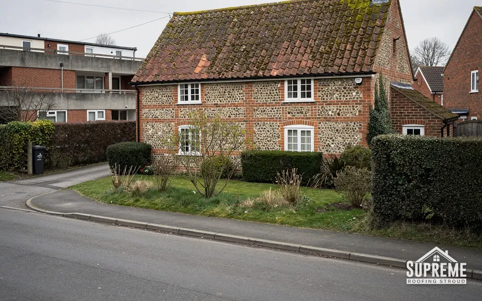 Flint and brick cottage with a clay tile roof beside a road
